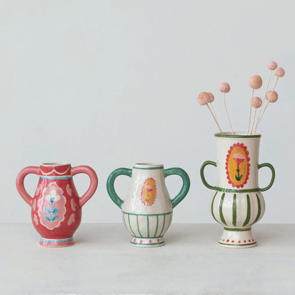 Three hand-painted stoneware urns with decorative flower handles and folk art patterns on a white surface.