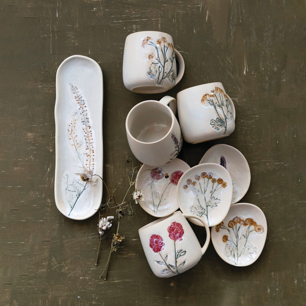 A collection of stoneware plates, mugs, and a long tray with floral designs arranged on a dark surface.