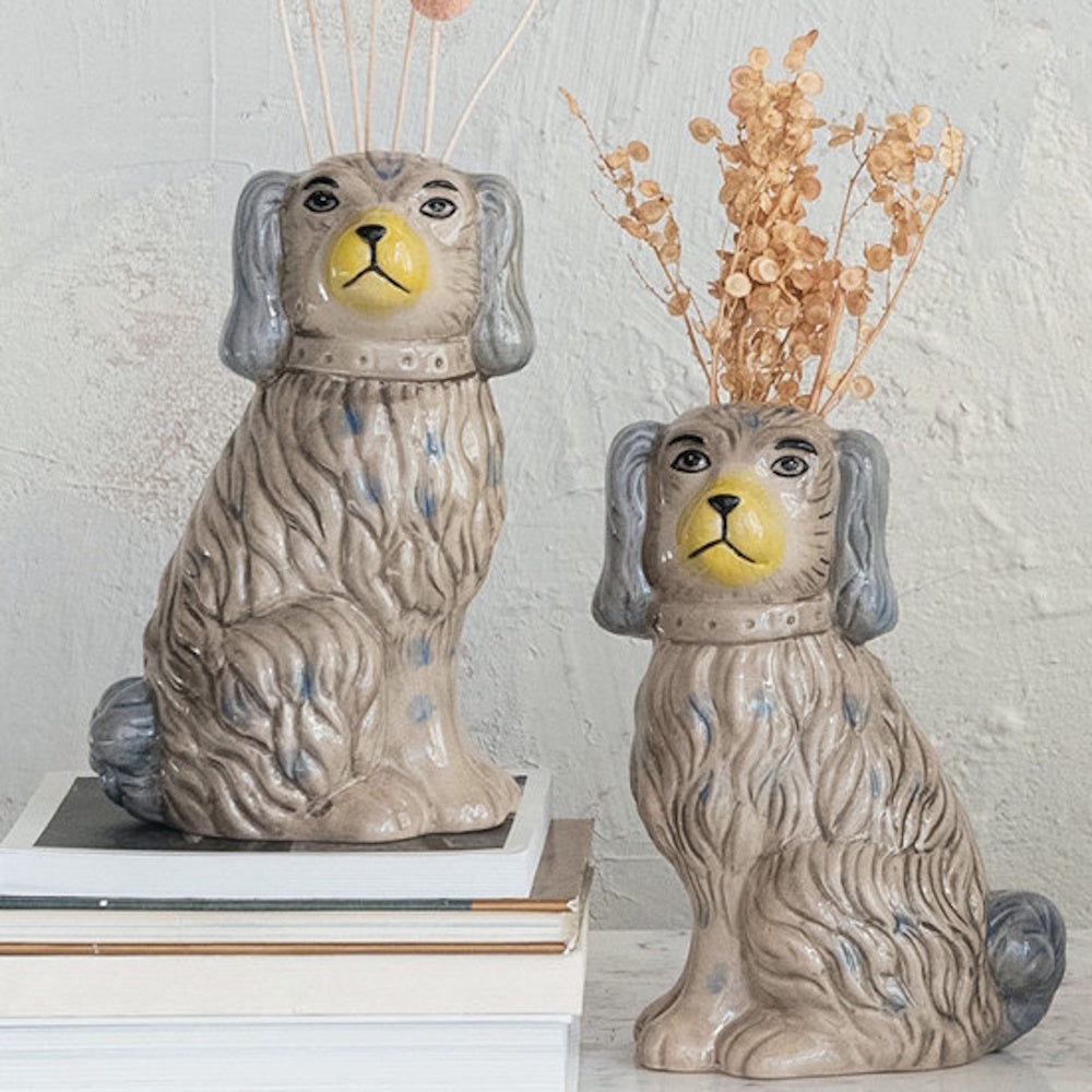 Two vintage-style spaniel dog vases with hand-painted blue spots and yellow noses, holding dried flowers on a stack of books.