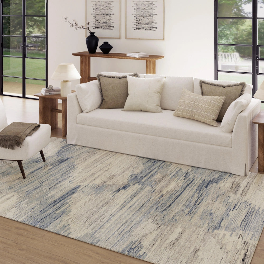 Blue and ivory abstract area rug in a modern living room with neutral sofa, wood furniture and natural light.