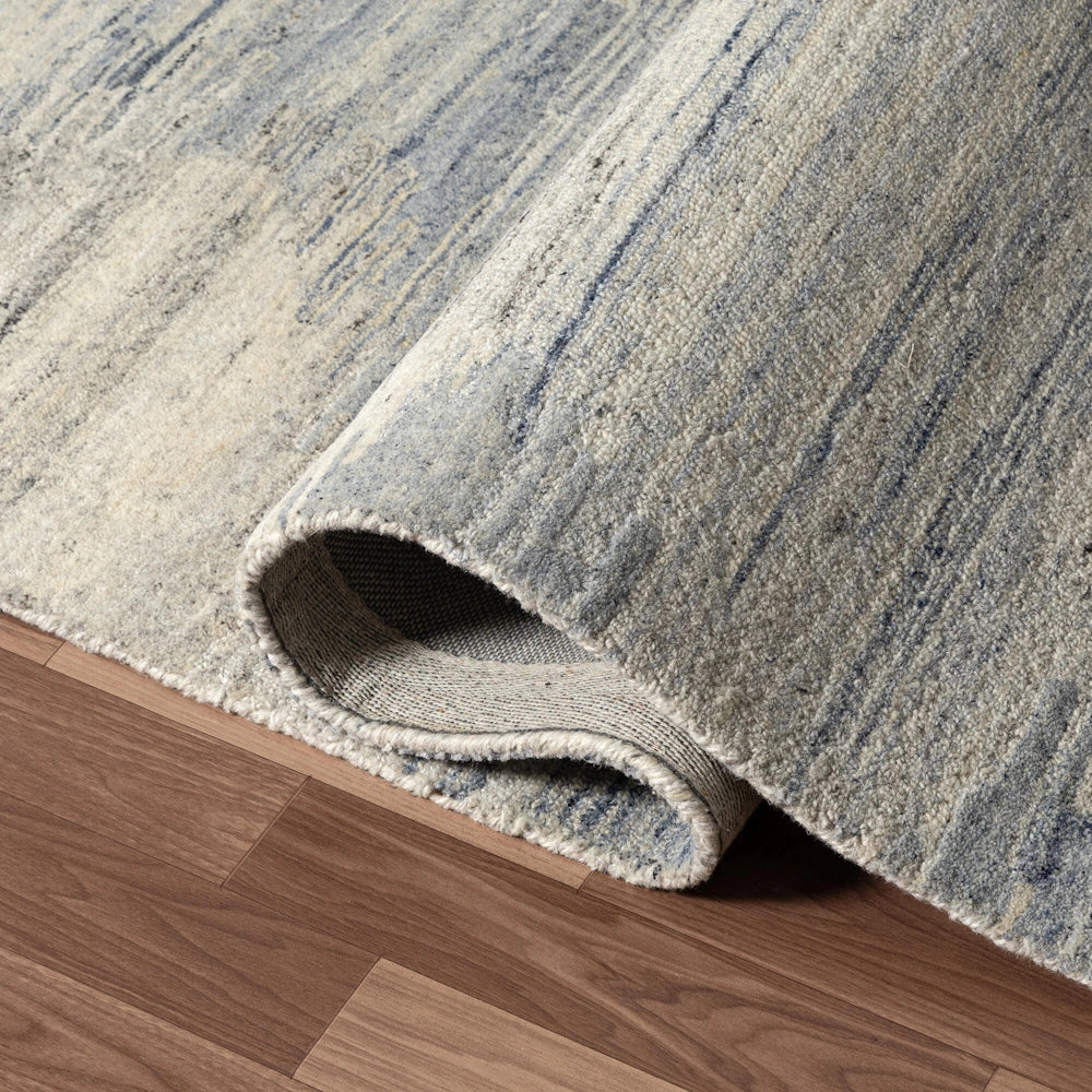 Close up of blue and ivory hand tufted rug corner showing textured pile, abstract pattern and folded edge detail.