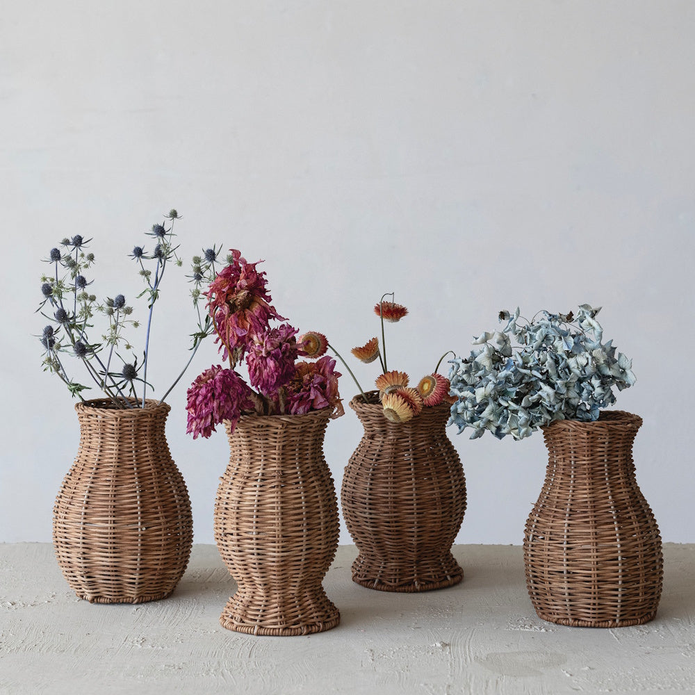 Four woven rattan vases filled with dried flowers styled on a rustic neutral surface.