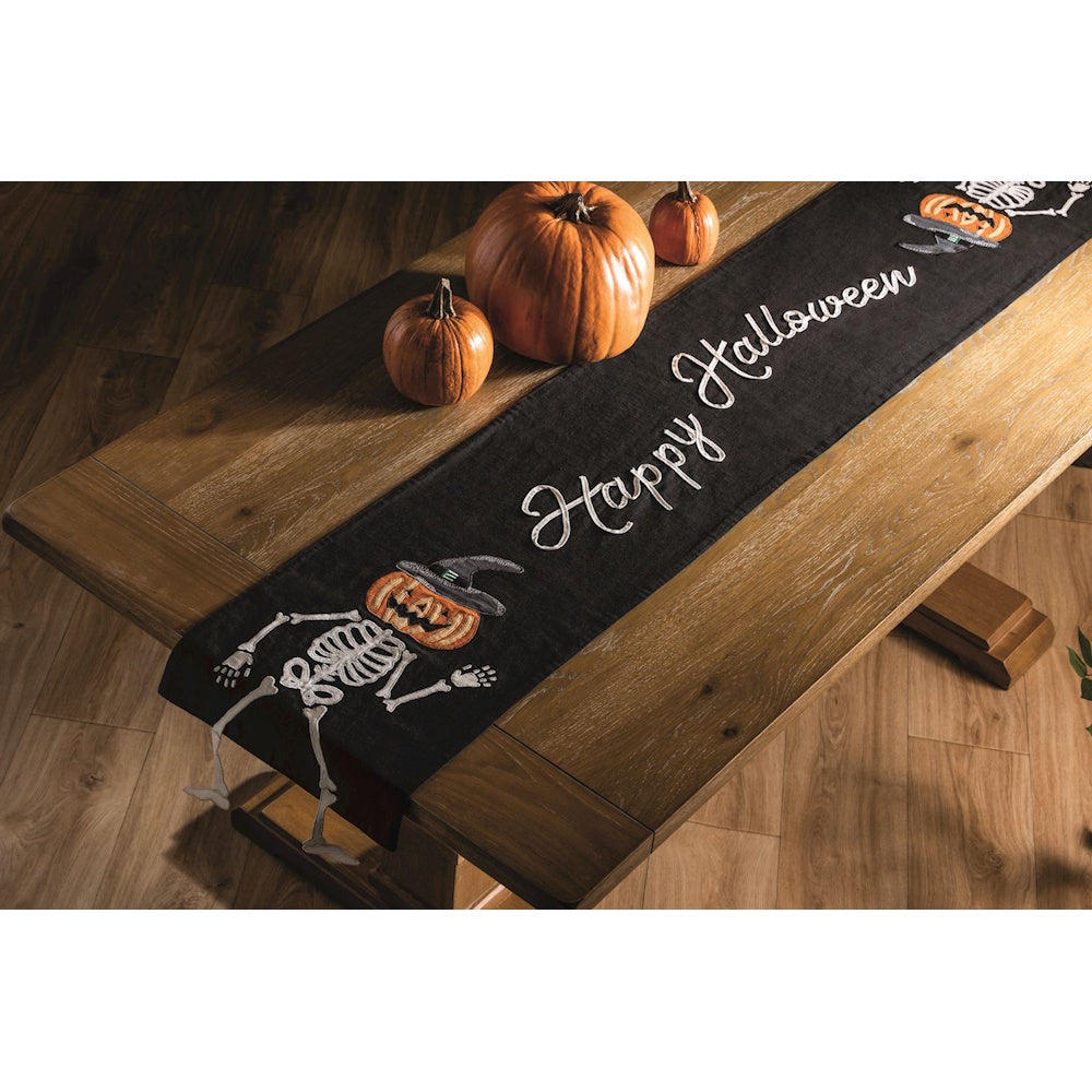 Black Happy Halloween table runner with skeleton pumpkin figures on a wooden table.