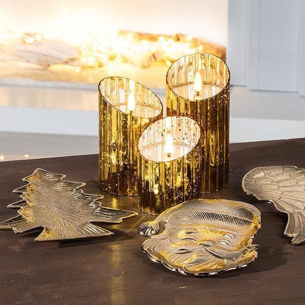 Gold Christmas dishes including a Santa face and tree, displayed beside lit gold glass candles.