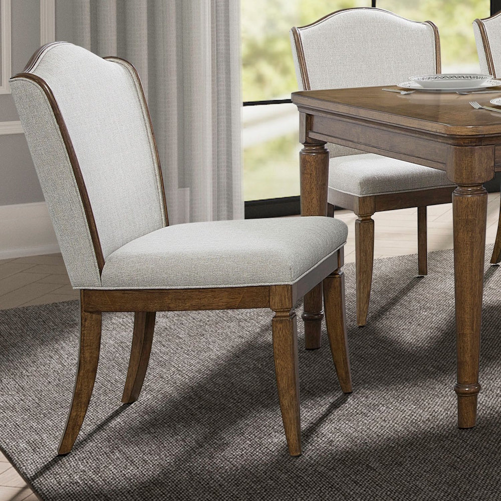 Light gray upholstered side chair with curved wooden legs and top frame set in a dining room with a wooden table.