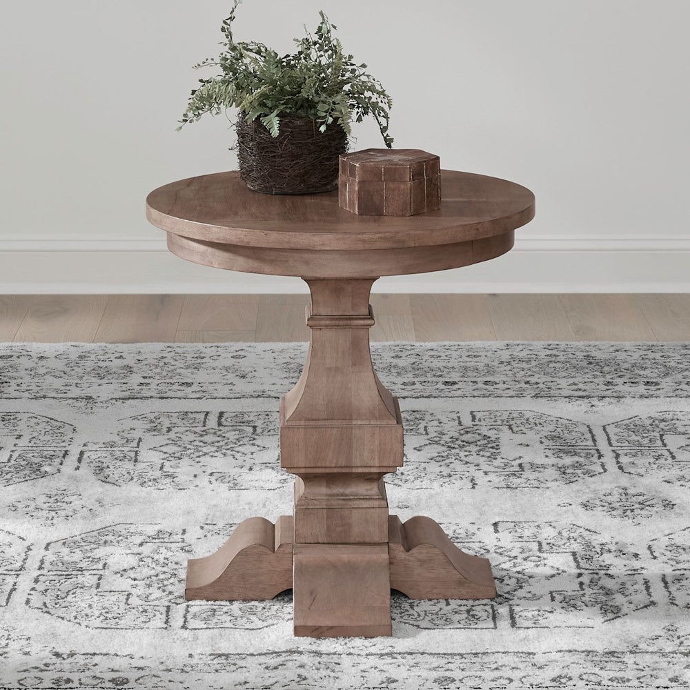 Round wooden end table with pedestal base styled with decor in a living room setting.
