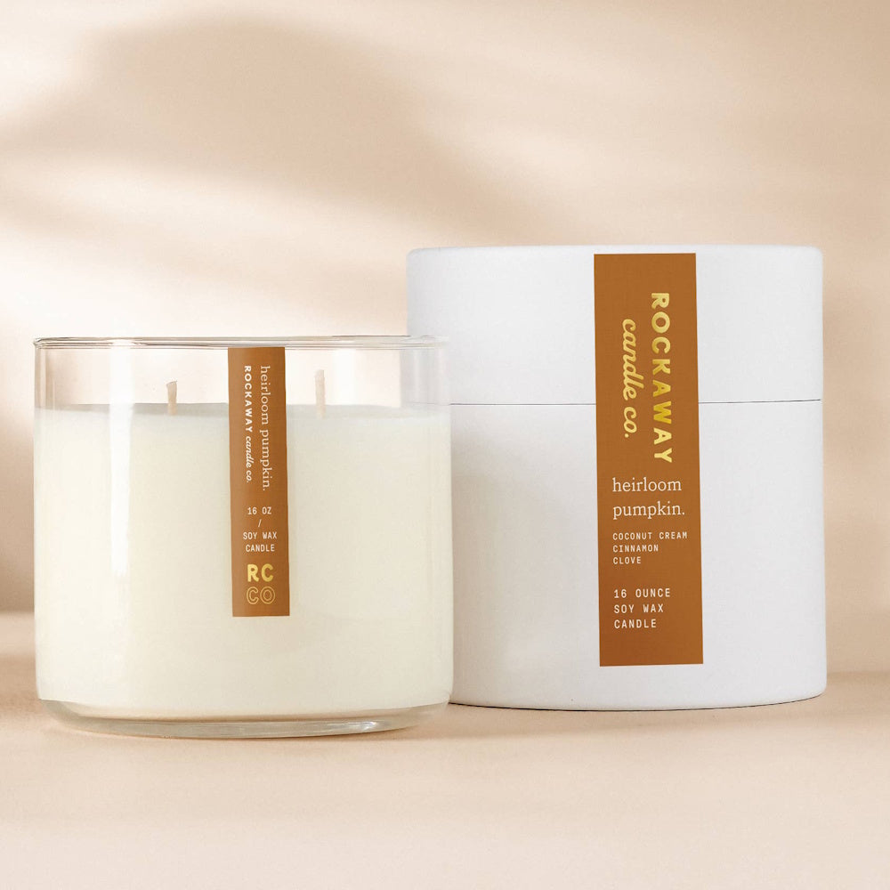 A 16 oz white soy wax candle in a clear glass jar next to its cylindrical white packaging tube.