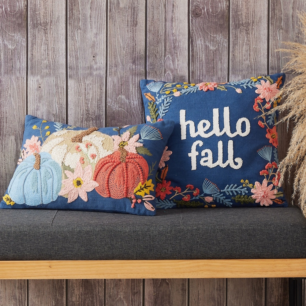 Two blue embroidered fall pillows on a grey bench against a wood wall. One says "hello fall".