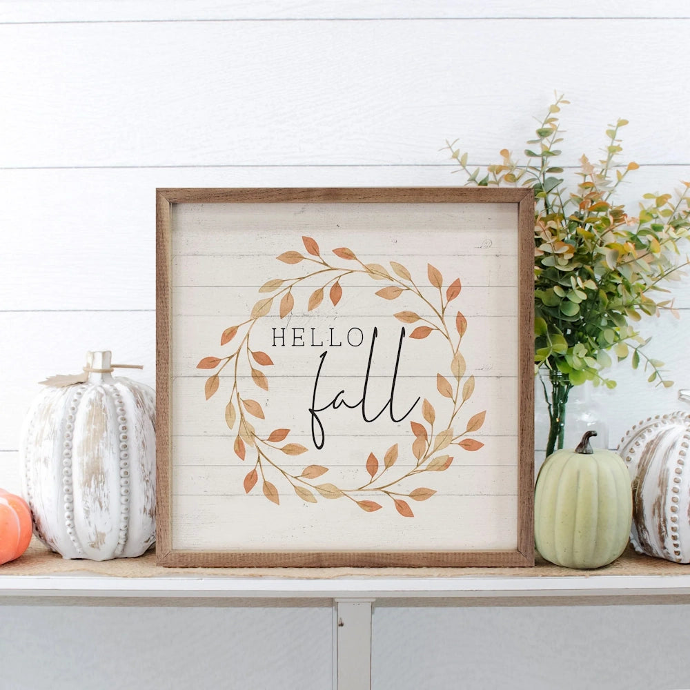 "HELLO fall" sign displayed on a shelf surrounded by decorative pumpkins and greenery.