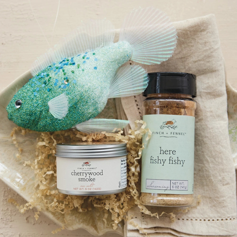 Finch + Fennel "here fishy fishy" seasoning and Cherrywood Smoke sea salt next to a decorative glittery fish.