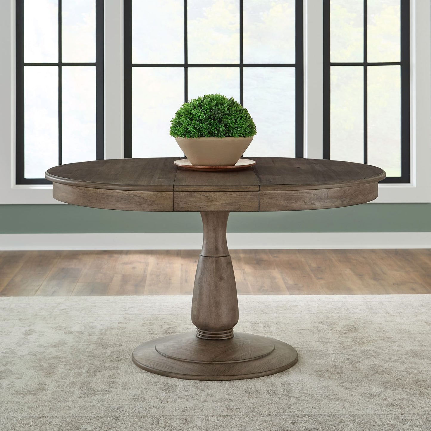 Round pedestal dining table in a rustic brown wood finish featuring a small potted green plant on top.
