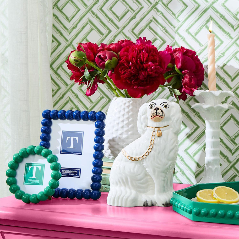 A colourful decor display featuring blue and green beaded photo frames alongside a ceramic dog figurine.