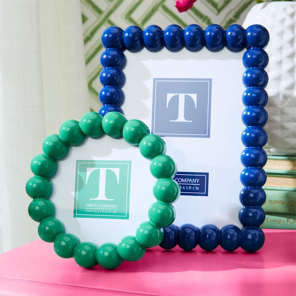 Round green and rectangular blue photo frames featuring beaded borders sit displayed on a bright pink surface.