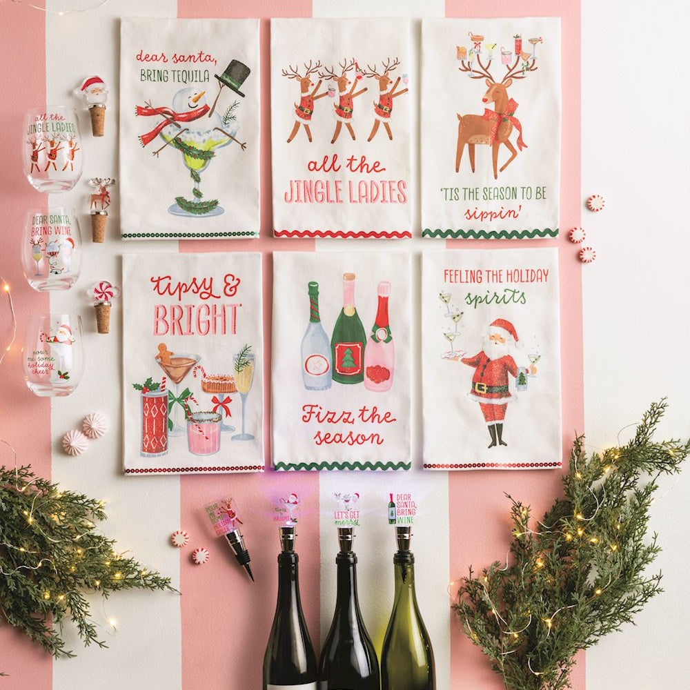 Six holiday-themed tea towels displayed with matching glasses, wine stoppers, and bottle pourers.