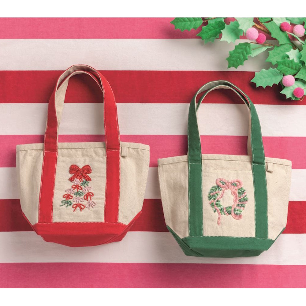Holiday beaded mini canvas tote bags displayed on a red and white striped background with green foliage.