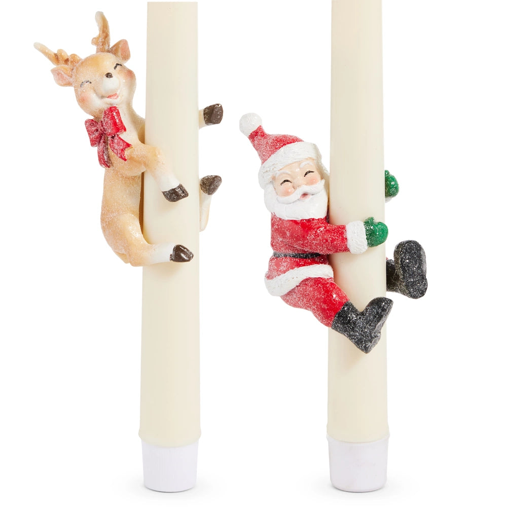 A reindeer and Santa Claus figurine hugging two tall ivory taper candles.