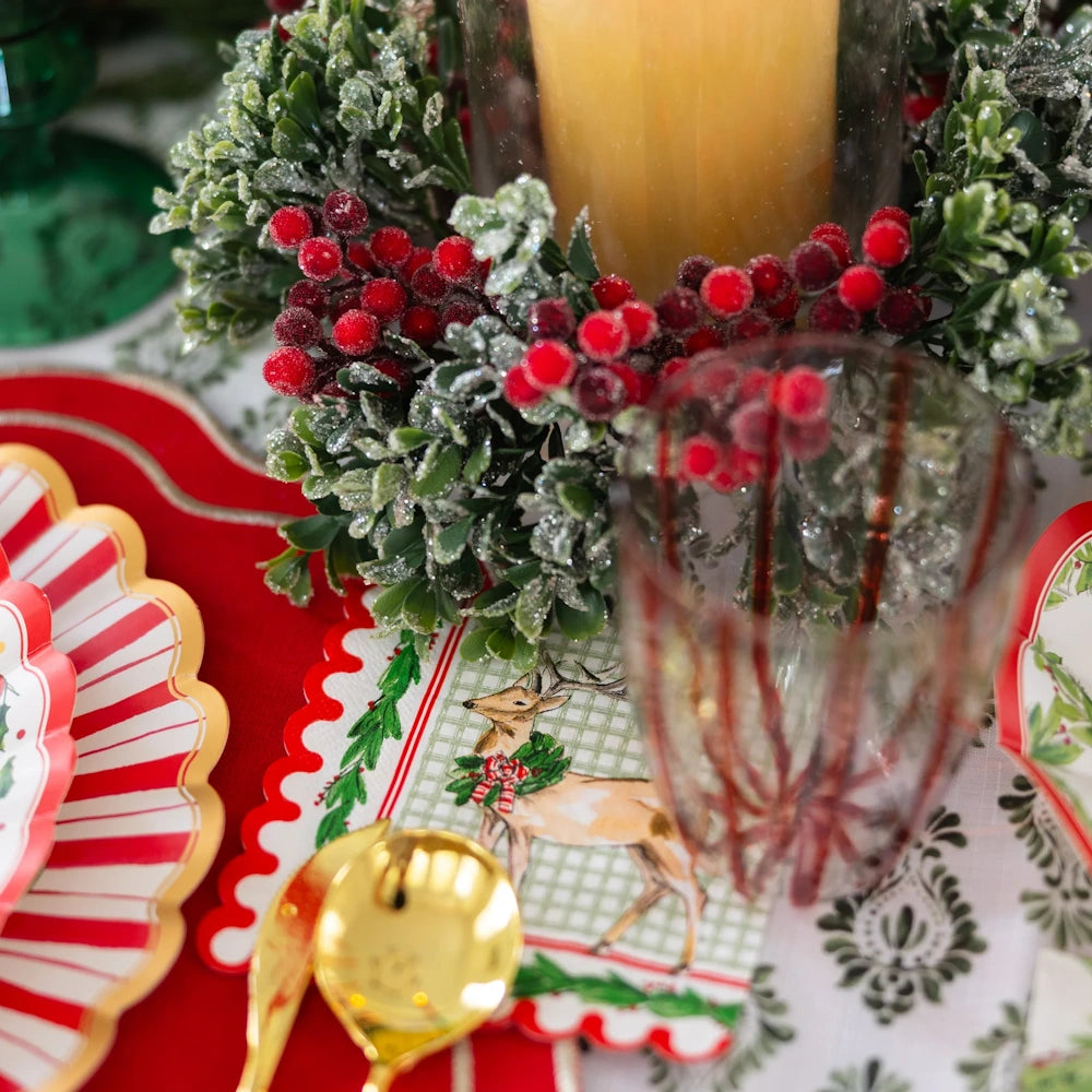 Overhead view of white paper cocktail napkins on a festive holiday table with red plates and gold flatware.