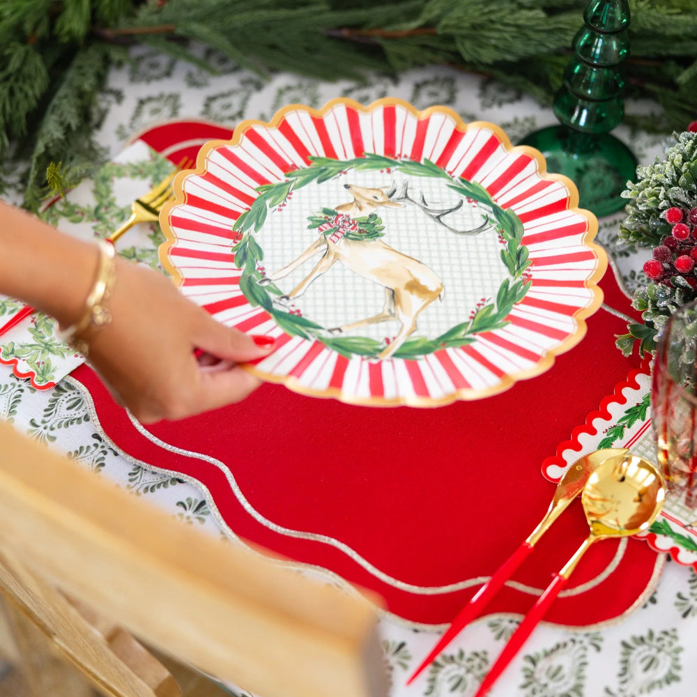 Angled view of a person holding a red, white, and gold paper dinner plate with a deer design.