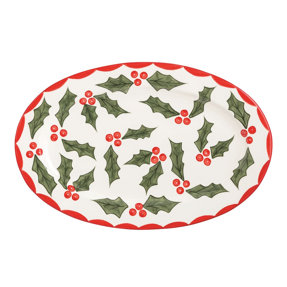 Oval ceramic platter decorated with green holly leaves, red berries, and a red scalloped rim.
