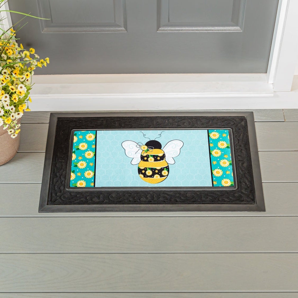 A doormat with a bumblebee on a light blue honeycomb background, framed by a black rubber border.
