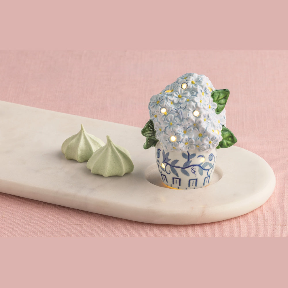 A light-up ceramic hydrangea in a blue and white patterned pot sits on a marble tray next to two green meringues.