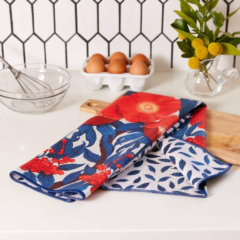 Icelandic poppy floral tea towel with red flowers and blue leaves on a kitchen counter near eggs and a whisk.