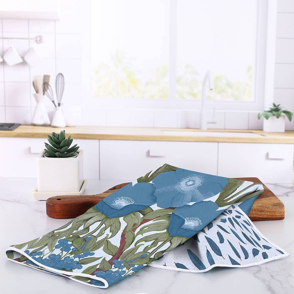 A floral kitchen tea towel with blue poppies draped over a wooden cutting board on a kitchen counter.