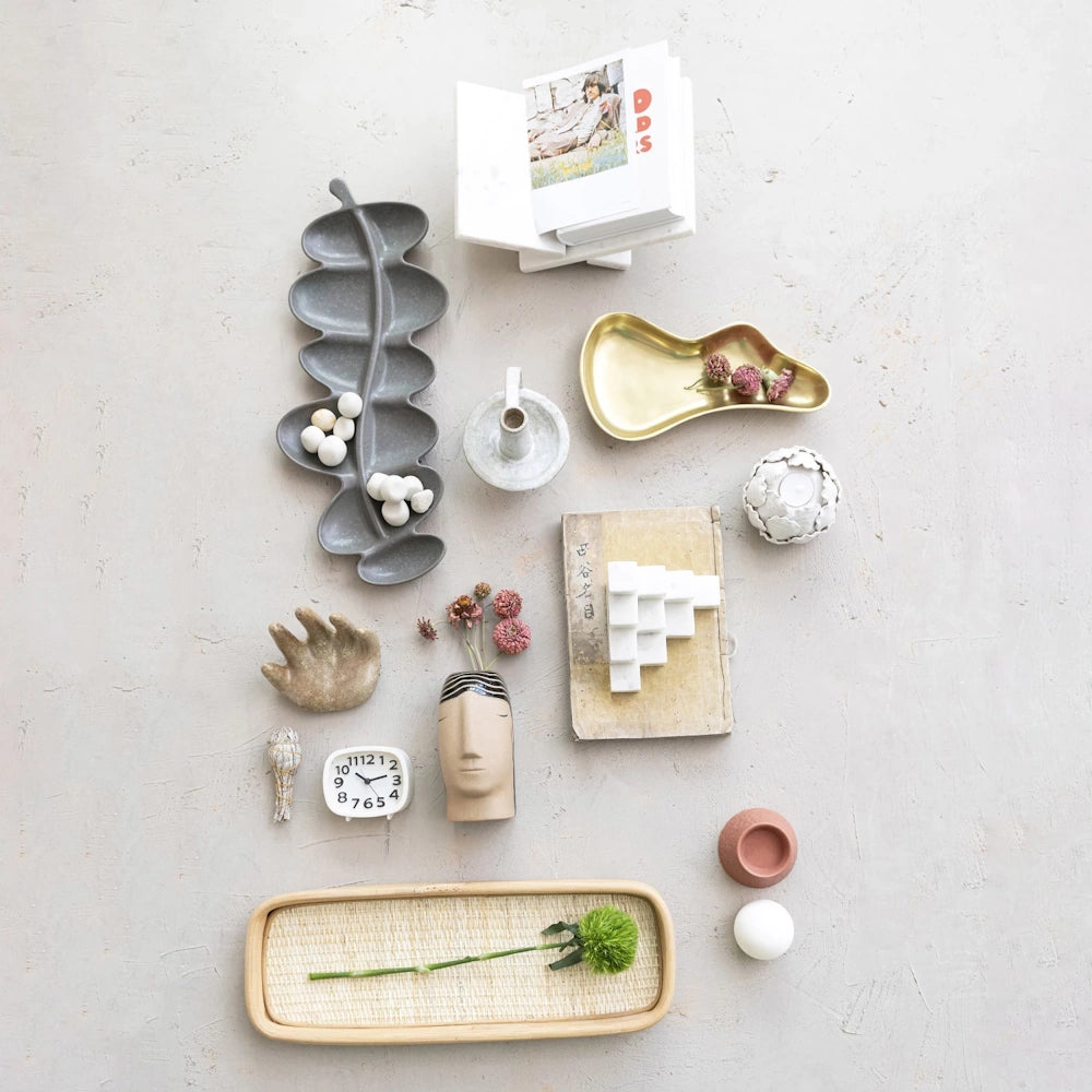Flat lay of modern home decor including a marble book holder, ceramic vases, and neutral trays on a textured surface.