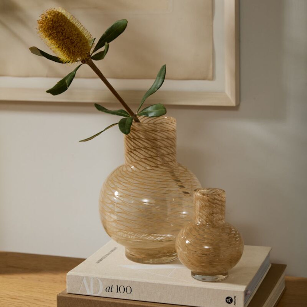 Two textured glass vases with a yellow Banksia flower sitting on "AD at 100" coffee table books.
