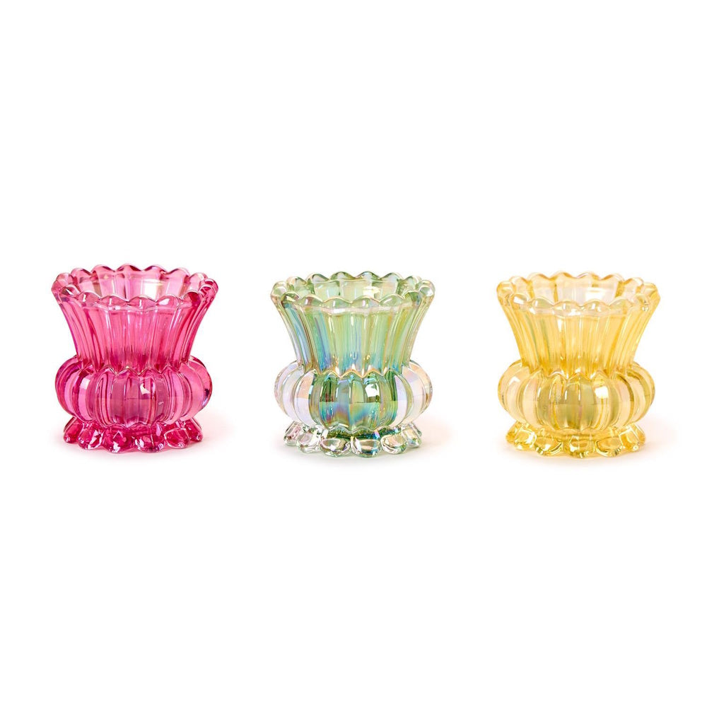 Three small ribbed, iridescent glass tealight holders or bud vases in pink, clear, and yellow on a white background.