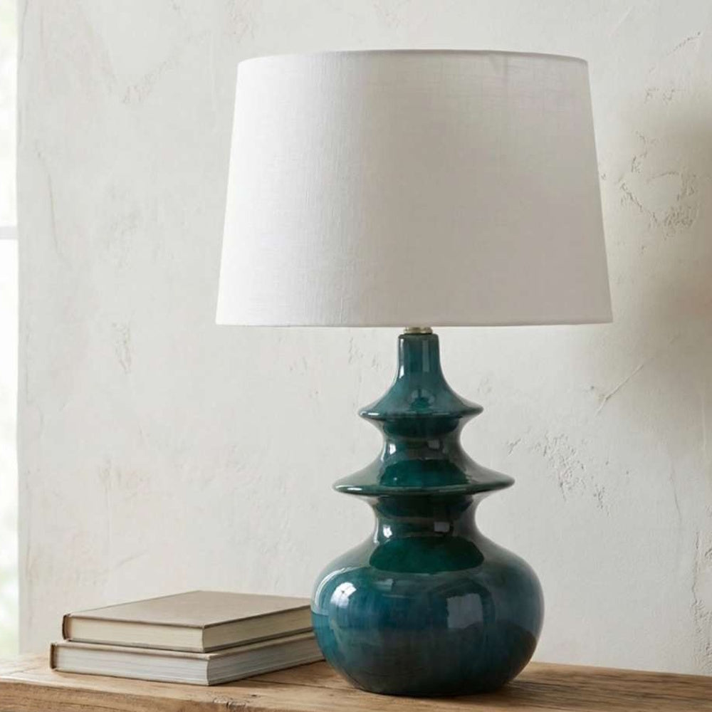 Teal glass table lamp on a wooden table next to two books against a textured plaster wall.