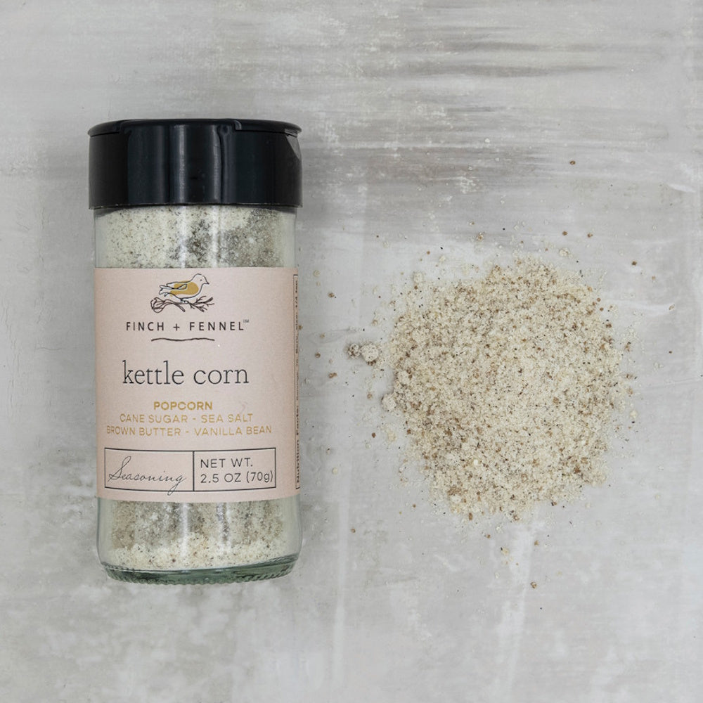 A Finch + Fennel Kettle Corn seasoning jar next to a small pile of spilled seasoning on a gray background.