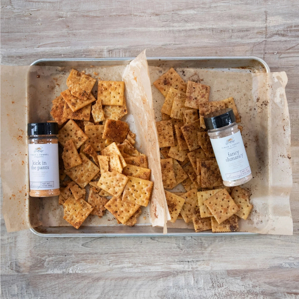 Baking sheet with seasoned crackers divided into two sections alongside Finch + Fennel spice jars.