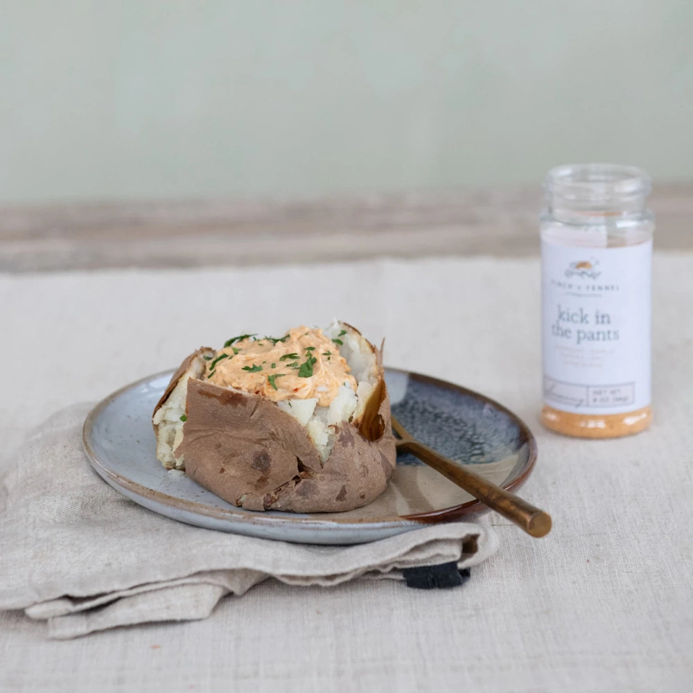 Baked potato topped with seasoned cream spread on a plate next to a Finch + Fennel seasoning jar.