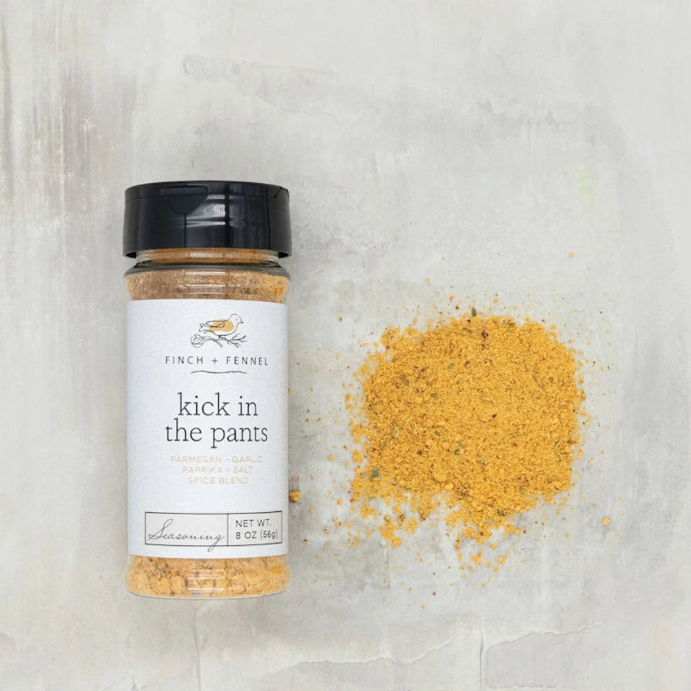 Finch + Fennel Kick in the Pants seasoning jar next to a pile of golden spice mix on a light background.