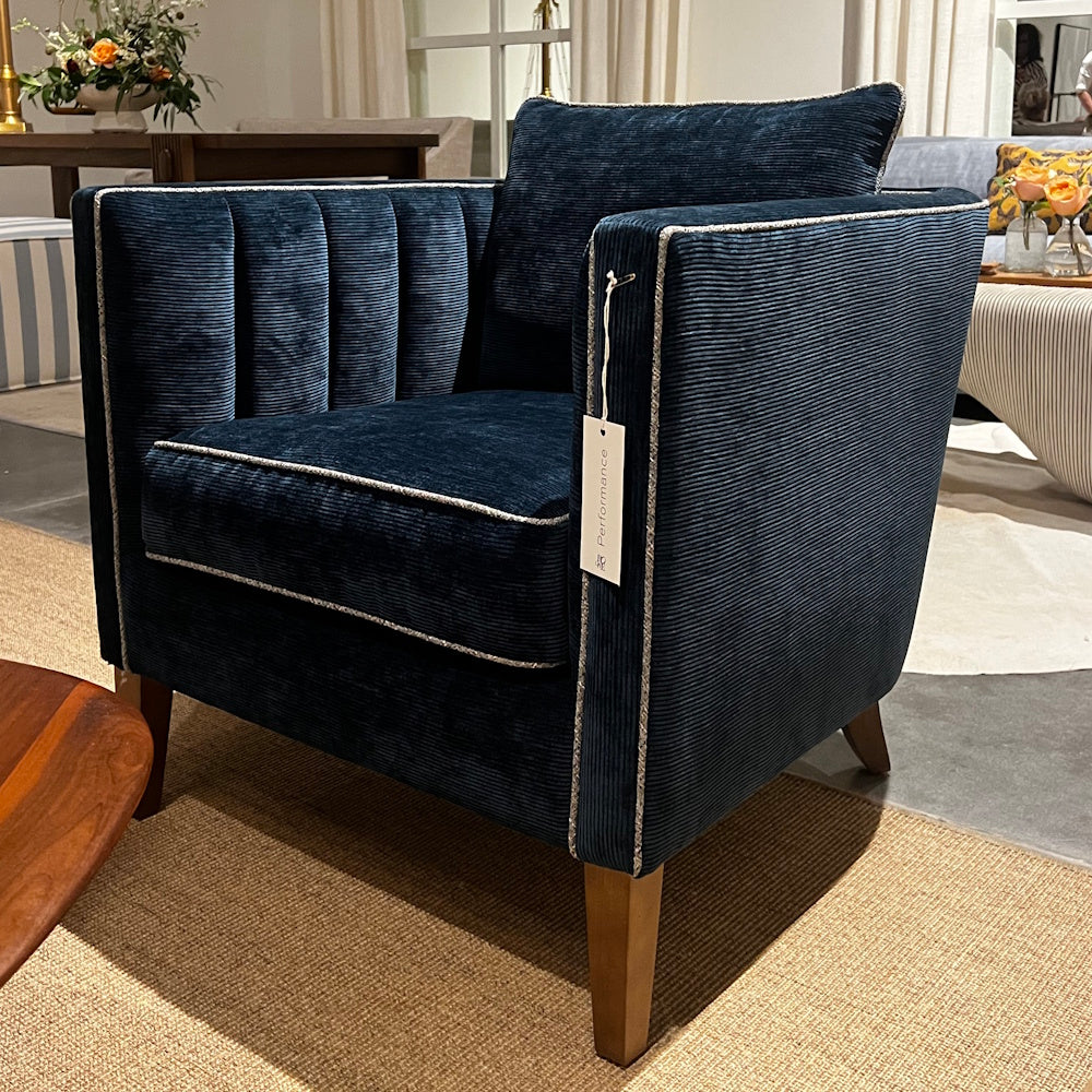 Blue velvet Kitt accent chair with channel tufting and wooden legs in a living room setup.