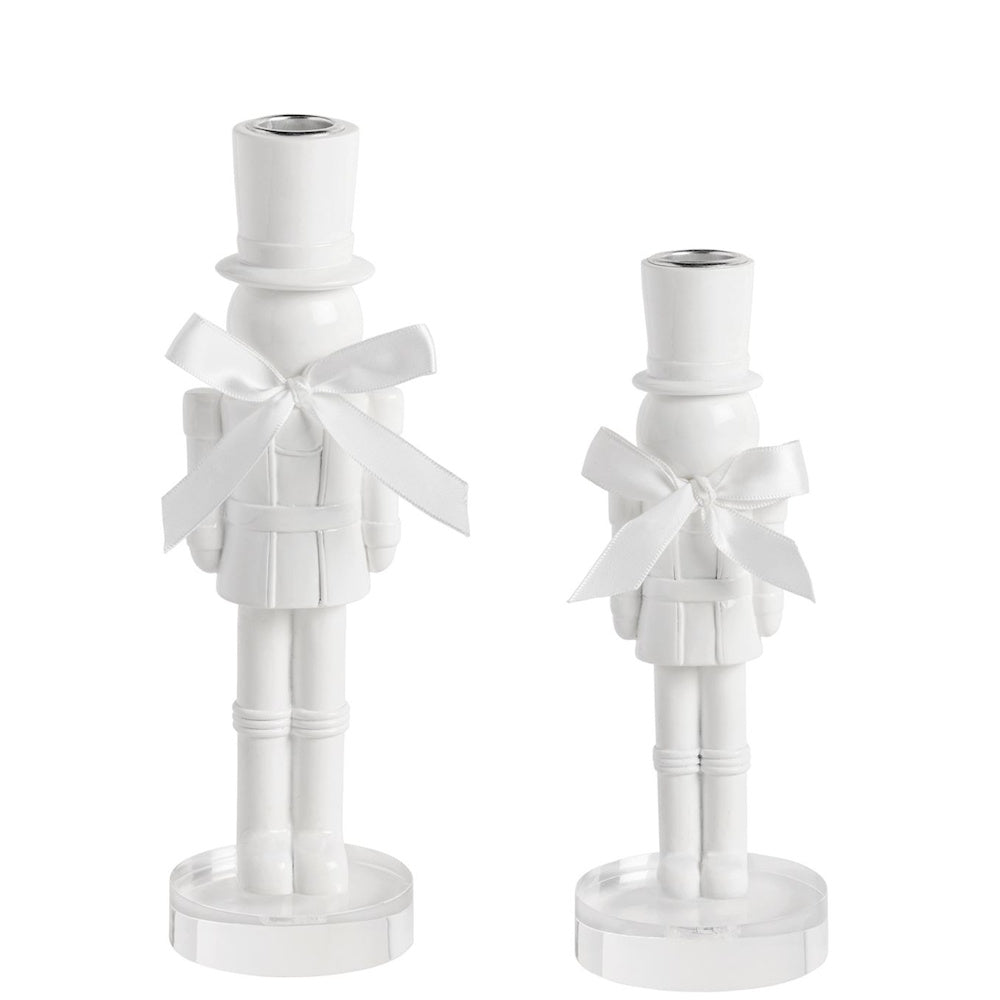 Pair of white lacquered nutcracker candlestick holders adorned with white satin bows on acrylic bases.