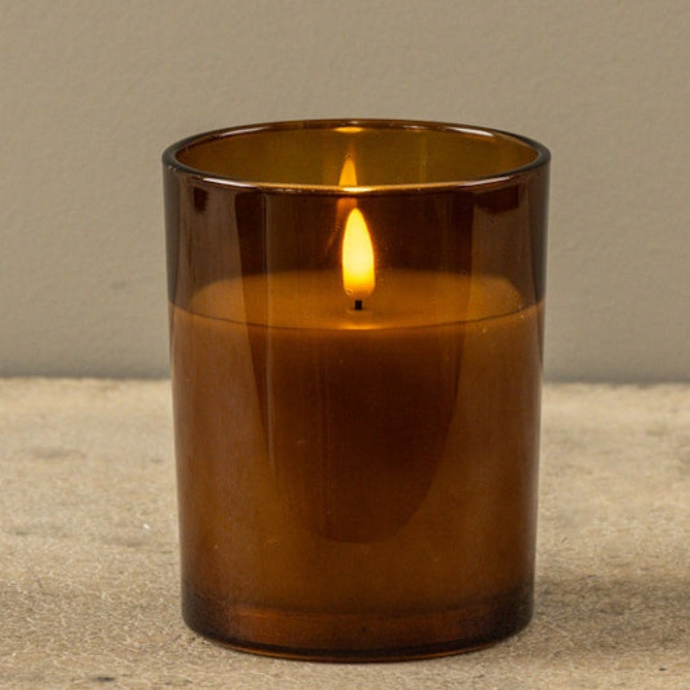 Lit flameless candle glowing inside an amber glass jar, resting on a textured surface.
