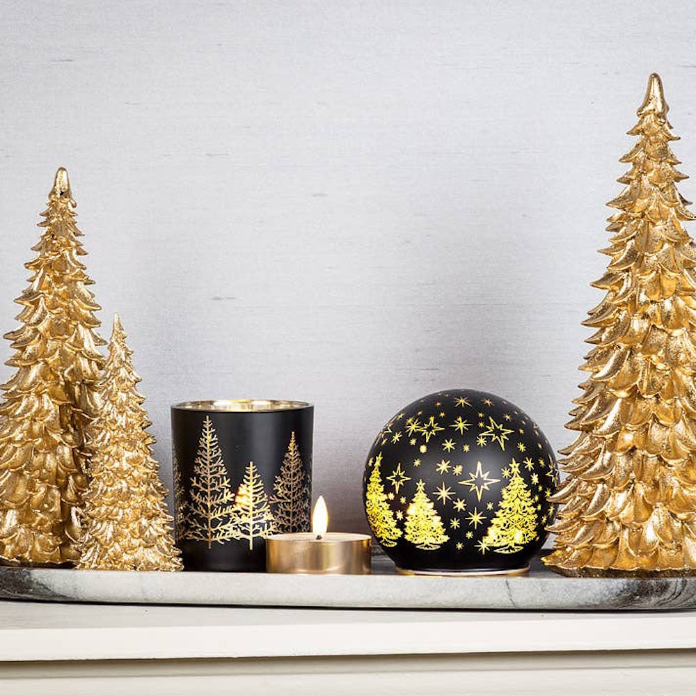 Black and gold candle holders and starry tree orb display set among textured gold Christmas trees.