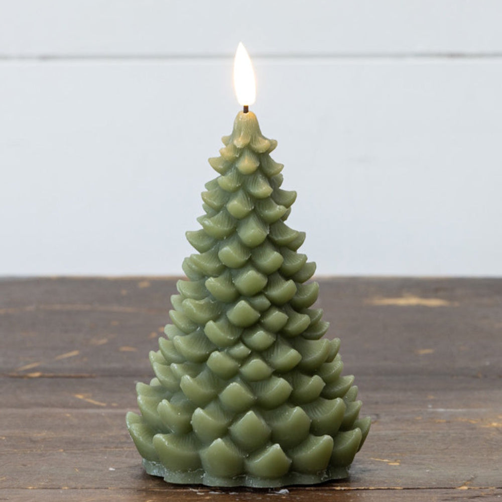 A dark green candle shaped like a pine tree with a glowing flame, standing on a rustic wooden surface.