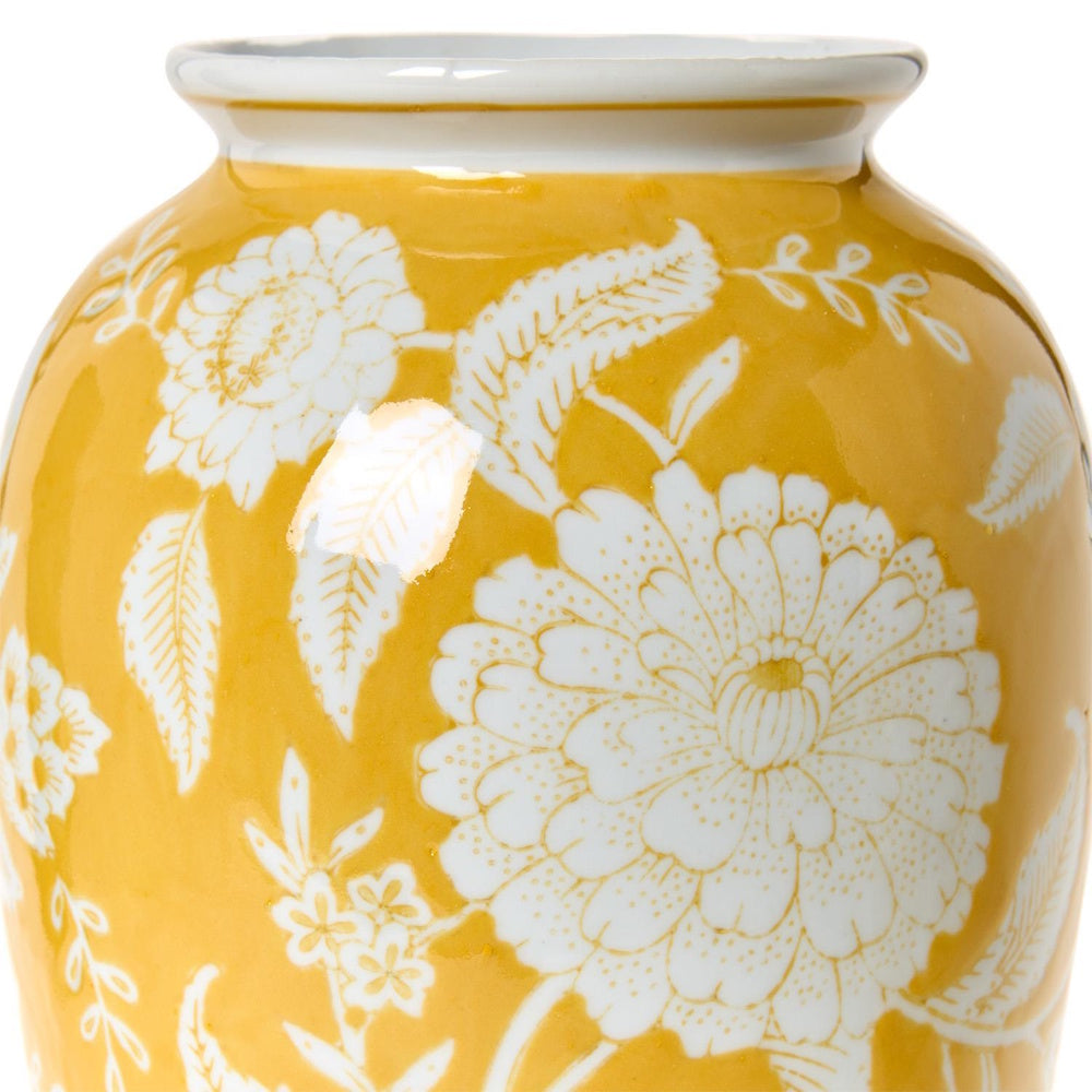 Close-up of a bright yellow ceramic vase featuring detailed white floral and leaf patterns.