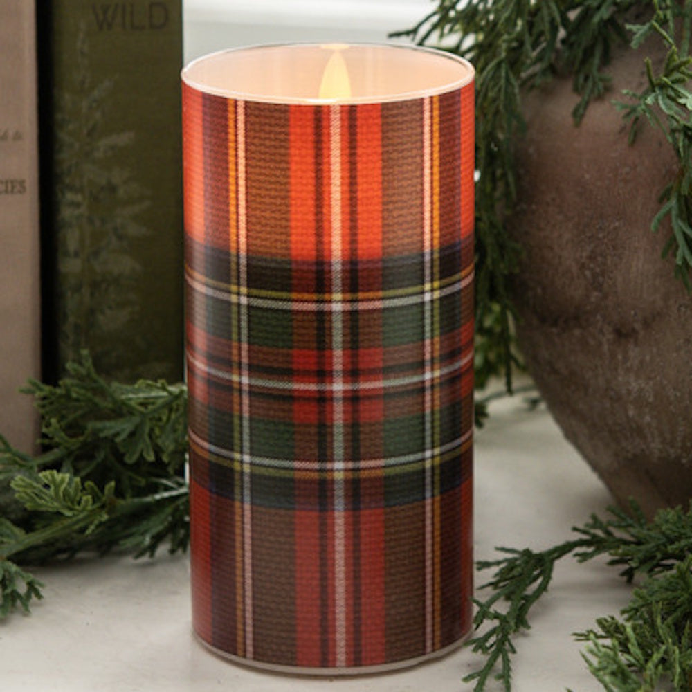 Flameless pillar candle with a red, green, and white tartan plaid cylinder cover and glowing flame.
