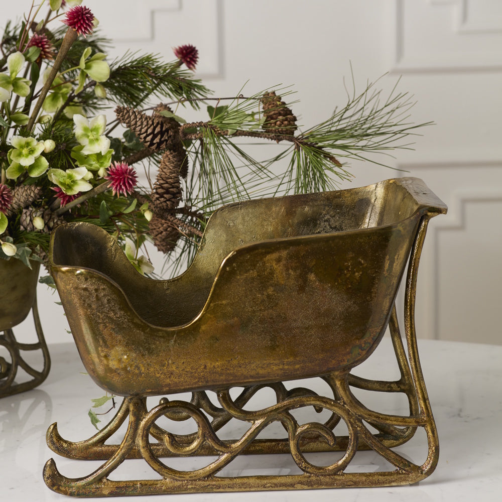 Vintage antique gold sleigh planter with ornate scrollwork runners.