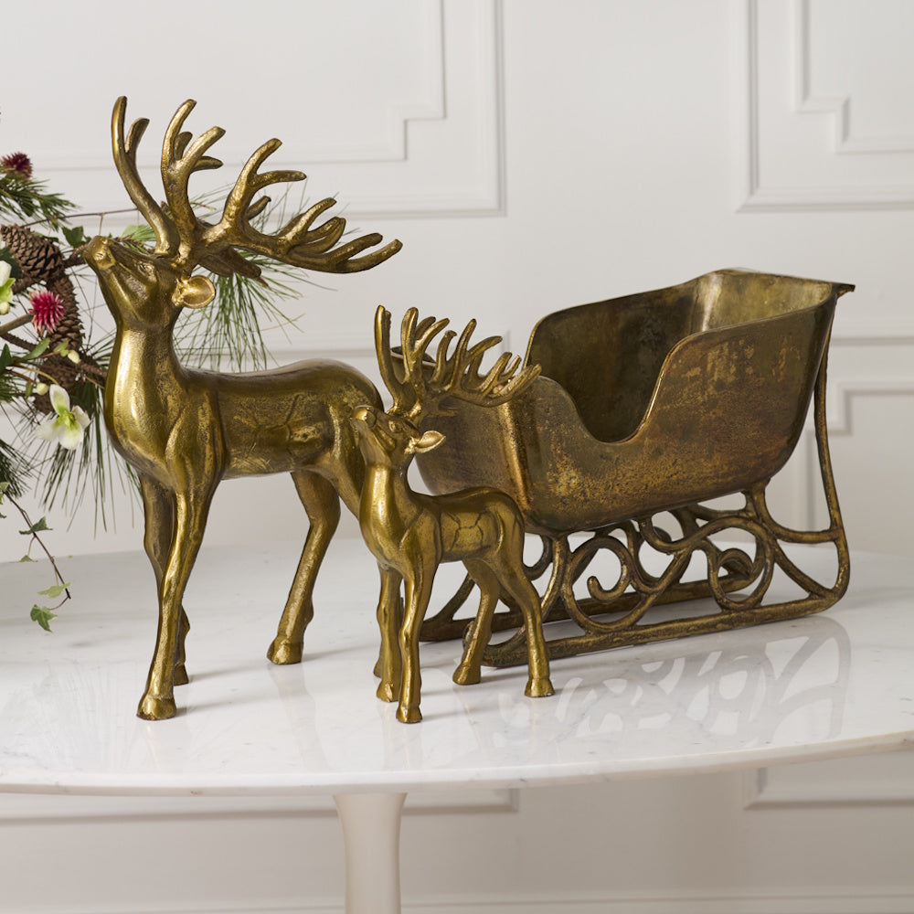 Two vintage brass deer statues standing next to a matching decorative brass sleigh planter.