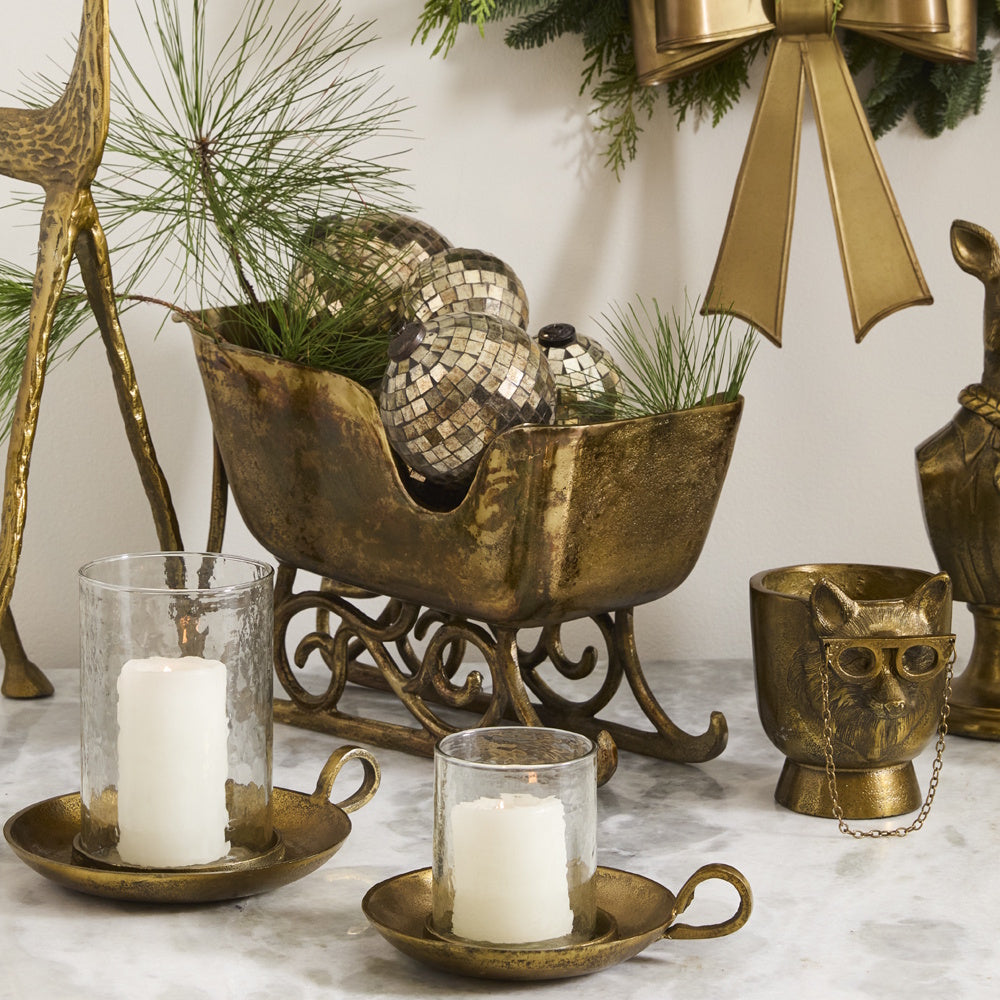 Vintage brass sleigh planter with festive disco ball ornaments, greenery, and glowing candles.