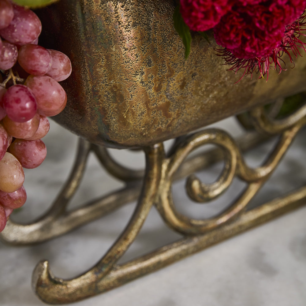Vintage bronze sleigh planter holding red grapes and vibrant red flowers.