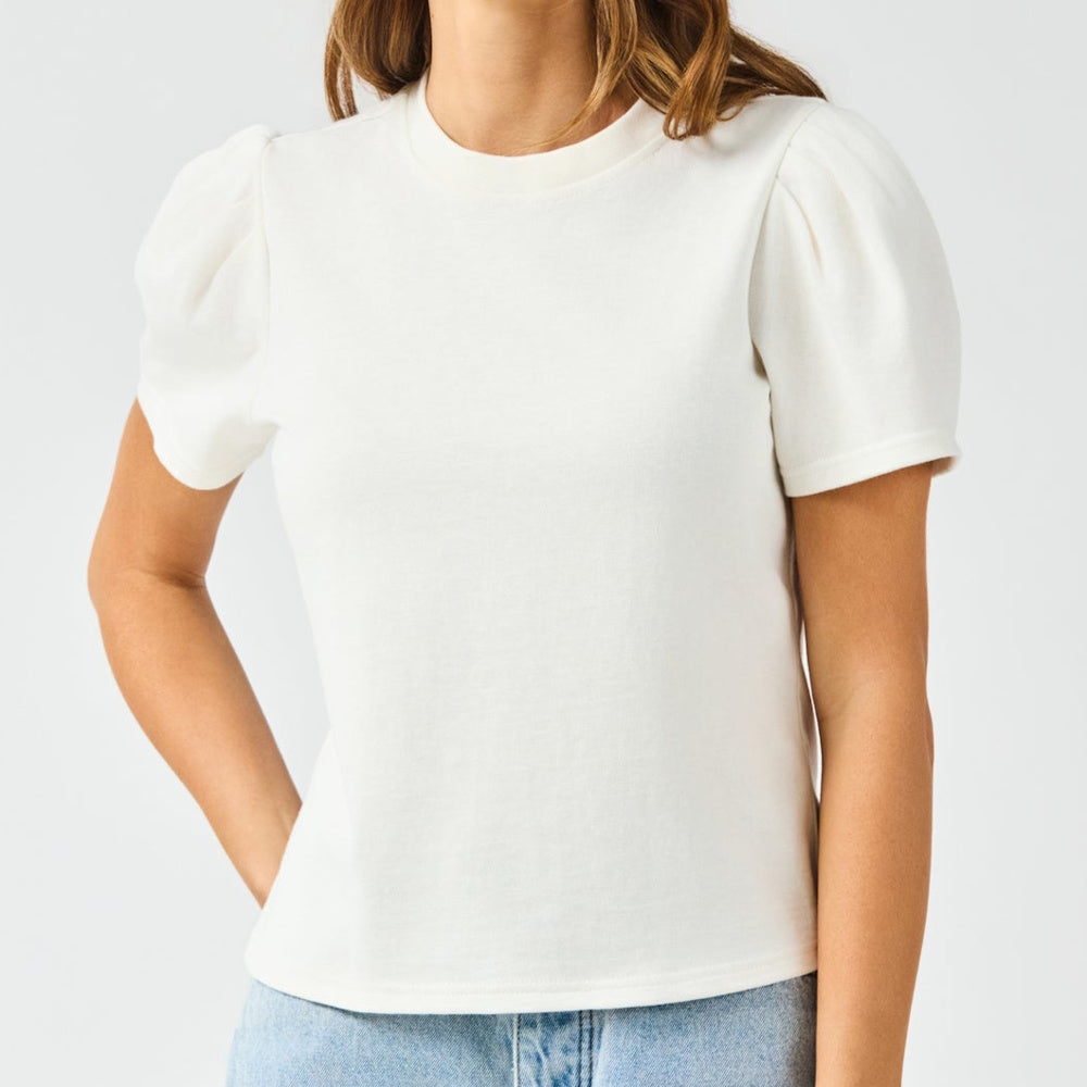 White short-sleeve crewneck top with puffed, pleated shoulders worn with light-wash denim.