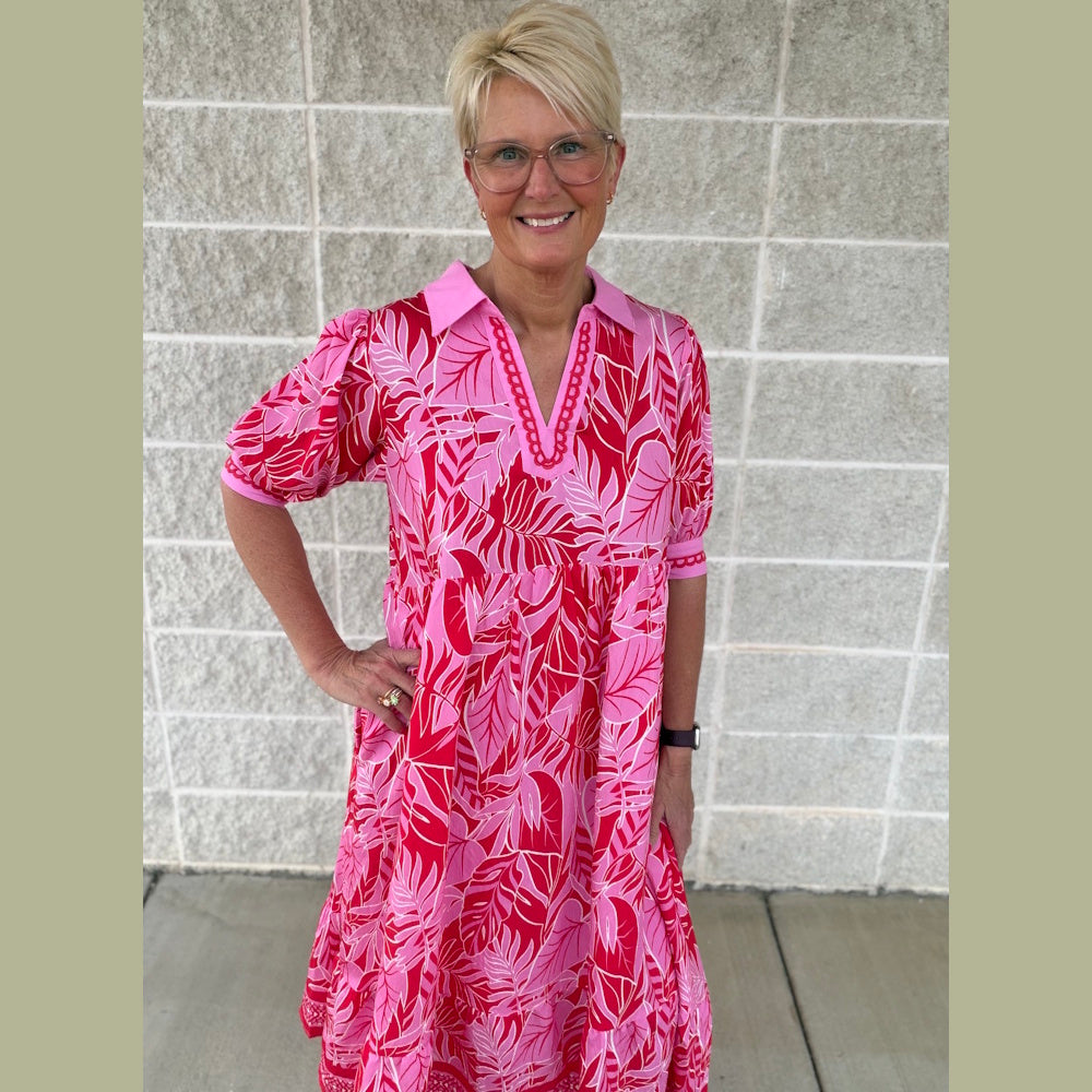 Woman with blonde hair wearing a pink and red leaf-print midi dress with a collar and short sleeves.