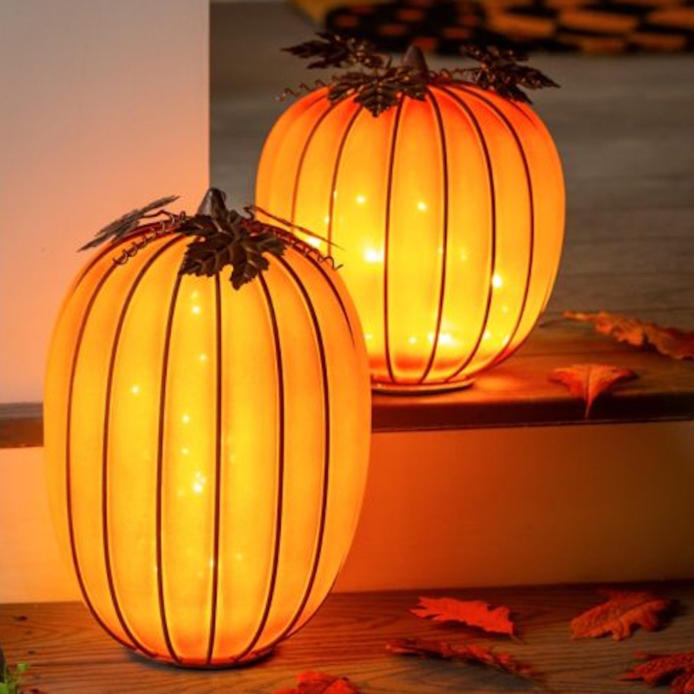 Two glowing orange glass pumpkin lanterns with metal leaf accents on wooden steps.