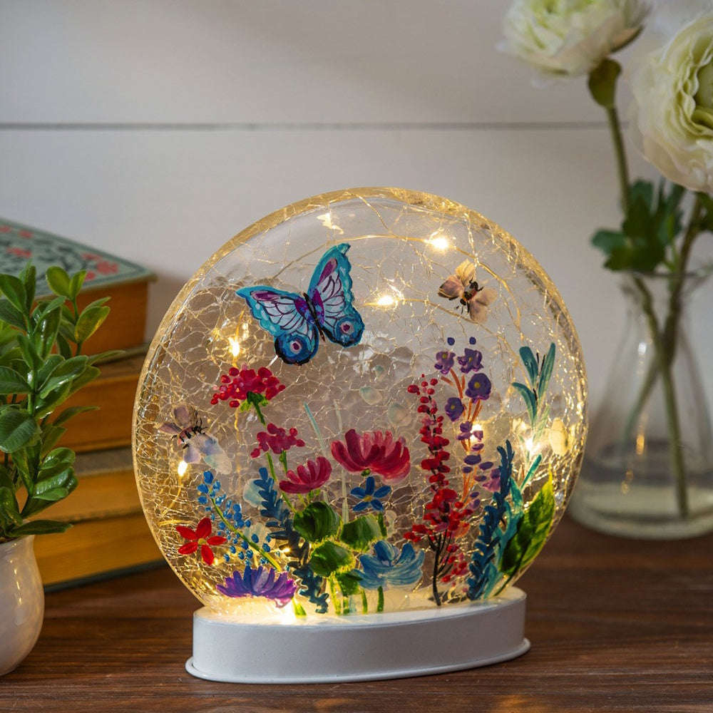 A lighted crackle-glass disc lamp painted with a blue butterfly, bees, and colorful spring flowers.